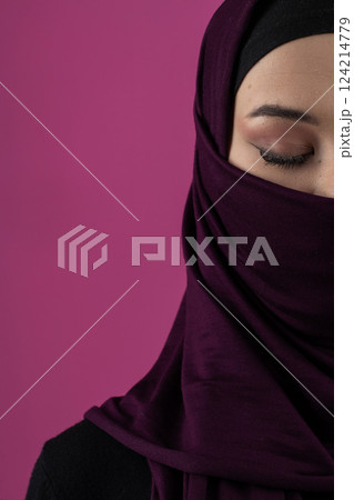 Beautiful Muslim woman in a hijab posing elegantly in a studio with a pink background. 124214779