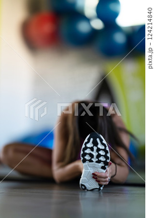 Woman Stretching in Gym. A athletic woman wearing a purple sports outfit is stretching her legs in a gym. Woman Stretching in Gym. A athletic woman wearing a purple sports outfit is stretching her legs in a gym. 124214840