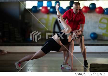 A trainer guides two women through stretching exercises in the gym, promoting flexibility, wellness, and a healthy lifestyle. 124214893