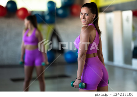 A focused and determined woman performs a strength building dumbbell workout at the gym, showcasing her athletic physique and dedication to fitness. 124215106