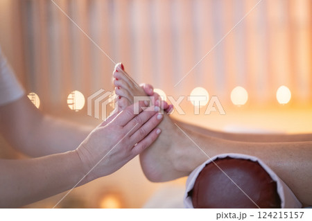 Foot Massage Therapy in a Relaxing Spa Setting. A professional massage therapist in a white uniform provides a soothing foot massage to a client in a calm and serene spa environment Foot Massage Therapy in a Relaxing Spa Setting. A professional massage therapist in a white uniform provides a soothing foot massage to a client in a calm and serene spa environment 124215157