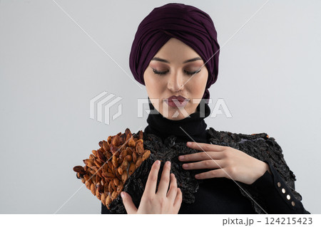A stylish Muslim woman in a hijab presents her innovative handmade fashion accessory crafted from dried plums in a professional studio. 124215423
