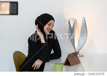 Modern Muslim woman in a hijab working on a tablet at home. 124215579