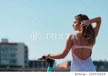 An elegant, stunning woman in a pink dress and sunglasses strikes a confident pose next to her electric scooter, radiating style and sophistication in the vibrant urban environment. An elegant, stunning woman in a pink dress and sunglasses strikes a confident pose next to her electric scooter, radiating style and sophistication in the vibrant urban environment. 124215619
