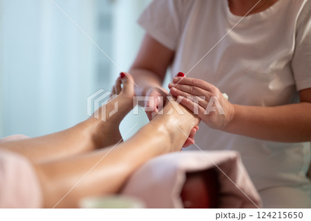 Foot Massage Therapy in a Relaxing Spa Setting. A professional massage therapist in a white uniform provides a soothing foot massage to a client in a calm and serene spa environment 124215650