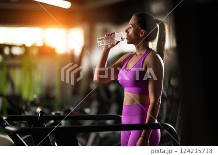 A fit woman resting after running on the treadmill and completing an intense conditioning workout, taking a moment to recover and recharge. 124215718