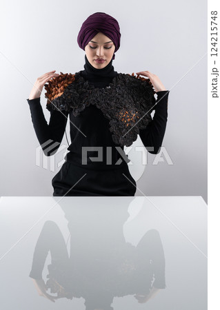 A stylish Muslim woman in a hijab presents her innovative handmade fashion accessory crafted from dried plums in a professional studio. A stylish Muslim woman in a hijab presents her innovative handmade fashion accessory crafted from dried plums in a professional studio. 124215748