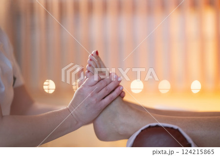 Foot Massage Therapy in a Relaxing Spa Setting. A professional massage therapist in a white uniform provides a soothing foot massage to a client in a calm and serene spa environment 124215865