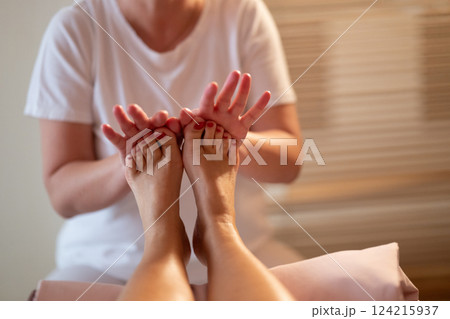 Foot Massage Therapy in a Relaxing Spa Setting. A professional massage therapist in a white uniform provides a soothing foot massage to a client in a calm and serene spa environment 124215937