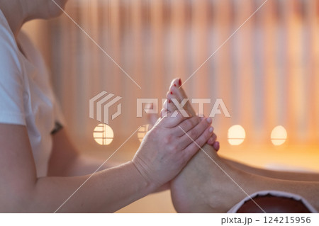 Foot Massage Therapy in a Relaxing Spa Setting. A professional massage therapist in a white uniform provides a soothing foot massage to a client in a calm and serene spa environment Foot Massage Therapy in a Relaxing Spa Setting. A professional massage therapist in a white uniform provides a soothing foot massage to a client in a calm and serene spa environment 124215956