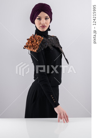 A stylish Muslim woman in a hijab presents her innovative handmade fashion accessory crafted from dried plums in a professional studio. 124215995