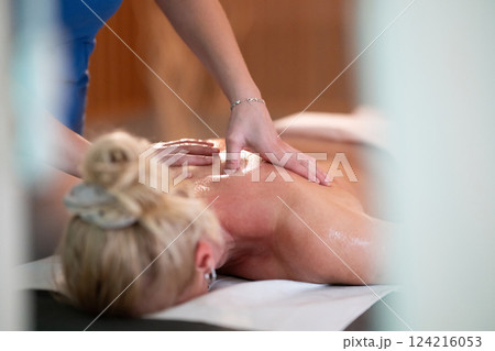 Relaxing Back Massage in a Spa Setting. A professional massage therapist in a blue uniform provides a relaxing back massage to a client lying on a massage table. 124216053