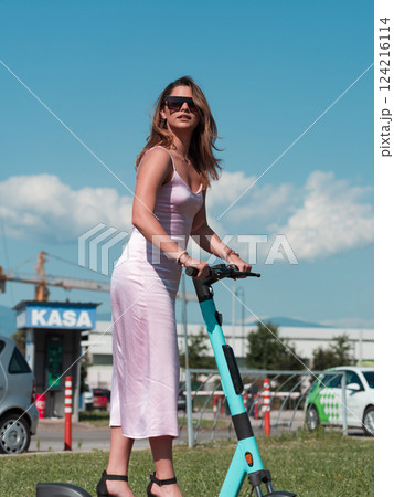 Elegant woman in a pink dress and sunglasses riding an electric scooter through the sunny city streets, embracing the freedom and style of a perfect urban adventure. 124216114