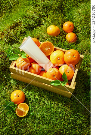 Brightly ripe Citrus Burst Orange placed on a green Meadow background. Unbranded tube of cream used for the design placed among fresh oranges in a wooden crate. Decorated with green orange leaves. 124216700