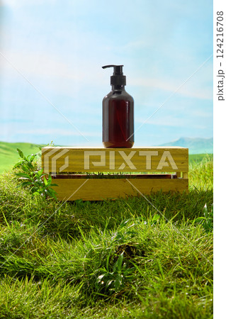 Amber pump bottle placed on a rectangular wooden crate presented in the middle of a green lawn. Blue sky background with misty mountains. Outdoor nature concept. Mockup bottle for design. Amber pump bottle placed on a rectangular wooden crate presented in the middle of a green lawn. Blue sky background with misty mountains. Outdoor nature concept. Mockup bottle for design. 124216708