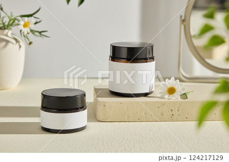 Close-up shot of two unlabeled jars on a stone pedestal, decorated with cute little flowers. The vase behind creates a highlight for the photo. Eco product presentation mockup. Advertising photo Close-up shot of two unlabeled jars on a stone pedestal, decorated with cute little flowers. The vase behind creates a highlight for the photo. Eco product presentation mockup. Advertising photo 124217129