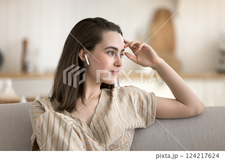 Portrait dreamy young female rest on sofa in wireless earbuds 124217624