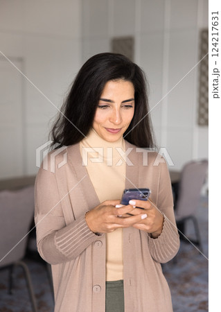 Focused Latina woman using smartphone standing in meeting room 124217631