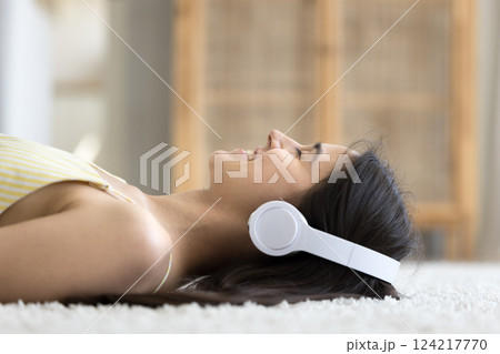 Closeup portrait smiling young female in headphones relaxing on carpet Closeup portrait smiling young female in headphones relaxing on carpet 124217770