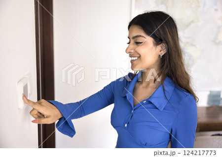 Young Indian woman adjusts temperature on digital thermostat 124217773
