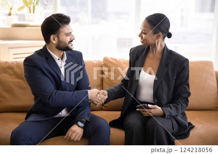 Two multiethnic colleagues shake hands met in company office lobby Two multiethnic colleagues shake hands met in company office lobby 124218056