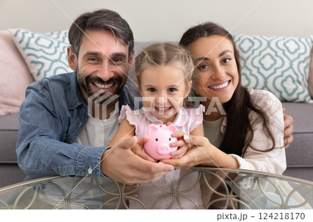 Happy mom and dad hugging little daughter kid holding piggybank 124218170