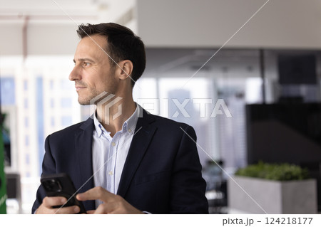 Positive handsome executive man using mobile phone in office alone Positive handsome executive man using mobile phone in office alone 124218177