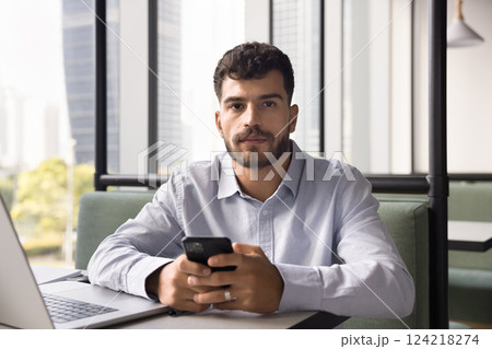 Man holding smartphone sit in co-working office with laptop 124218274