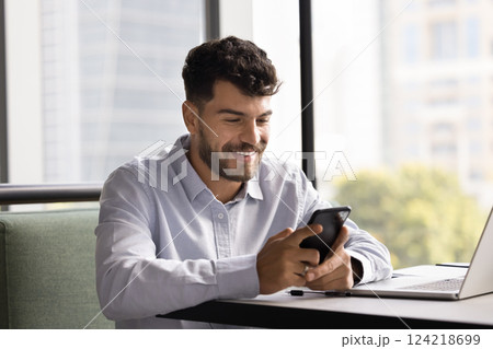Young man sitting at desk, smiling, looking at smartphone 124218699