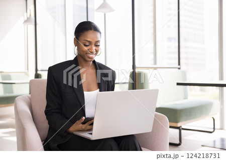 African businesswoman holding smartphone while working on laptop 124218731
