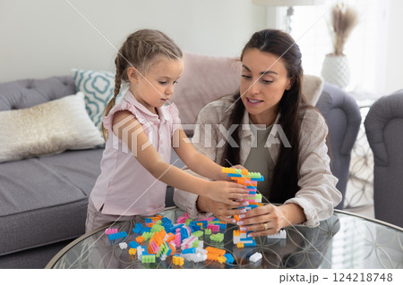 Caring young mother training preschooler daughter to build toy tower Caring young mother training preschooler daughter to build toy tower 124218748