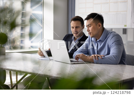 Two multiethnic businessmen using digital gadgets at workplace for teamwork Two multiethnic businessmen using digital gadgets at workplace for teamwork 124218798