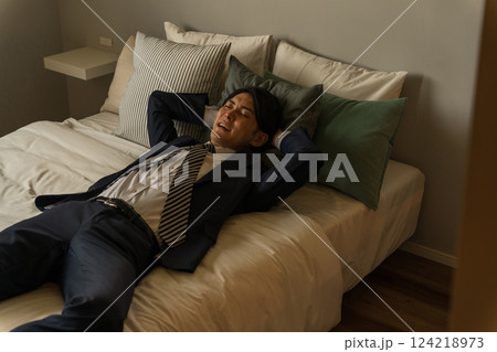 帰宅後スーツのままベッドで横になる若いアジア人男性ビジネスマン(残業・過労・社畜・体調不良) 帰宅後スーツのままベッドで横になる若いアジア人男性ビジネスマン(残業・過労・社畜・体調不良) 124218973