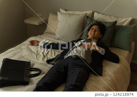 帰宅後スーツのままベッドで横になる若いアジア人男性ビジネスマン(残業・過労・社畜・体調不良) 帰宅後スーツのままベッドで横になる若いアジア人男性ビジネスマン(残業・過労・社畜・体調不良) 124218974