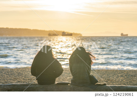 Two young girls enjoy the sunset at English Bay Beach, Vancouver City beautiful landscape. Concept of teenagers leisure. Two young girls enjoy the sunset at English Bay Beach, Vancouver City beautiful landscape. Concept of teenagers leisure. 124219061