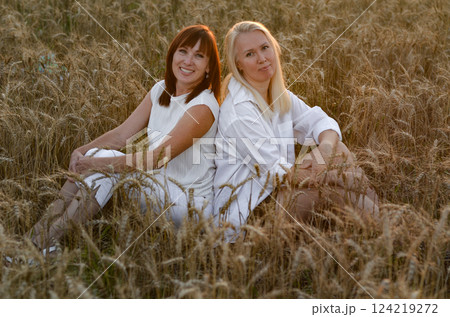 Two women enjoying a joyful moment in a golden wheat field during sunset while wearing bright summer outfits in a rural setting 124219272
