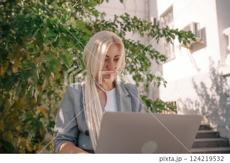 A woman is sitting on the ground with a laptop in front of her. She is wearing a gray jacket and a white shirt. A woman is sitting on the ground with a laptop in front of her. She is wearing a gray jacket and a white shirt. 124219532