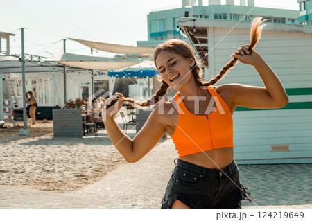 Woman Beach Summer Playful Pose: Happy girl playfully twirling braids near beach shacks during summer vacation. Woman Beach Summer Playful Pose: Happy girl playfully twirling braids near beach shacks during summer vacation. 124219649