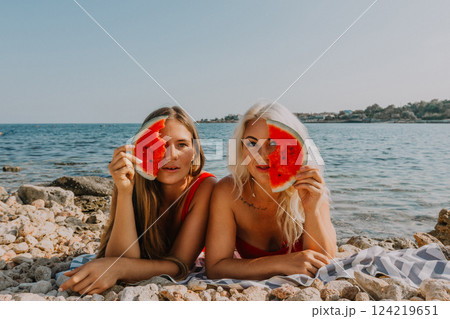 Watermelon Beach Summer: Two women playfully pose with watermelon slices on a sunny beach. 124219651