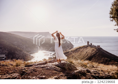 woman stands on a rocky hill overlooking a body of water. She is wearing a white dress and she is in a state of joy or celebration. Concept of freedom and happiness. woman stands on a rocky hill overlooking a body of water. She is wearing a white dress and she is in a state of joy or celebration. Concept of freedom and happiness. 124219668