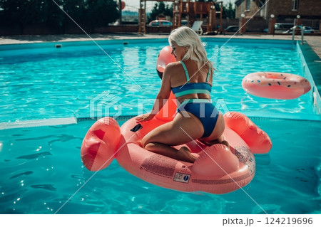 A woman is sitting on a pink inflatable raft in a swimming pool 124219696