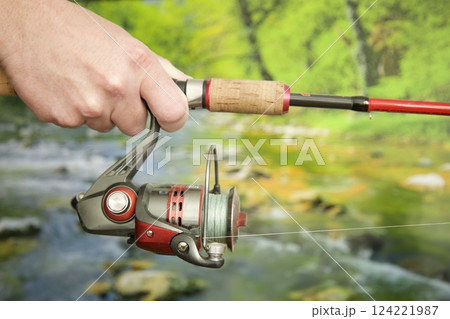 hands holding spinning rod against river background, spring summer fishing 124221987