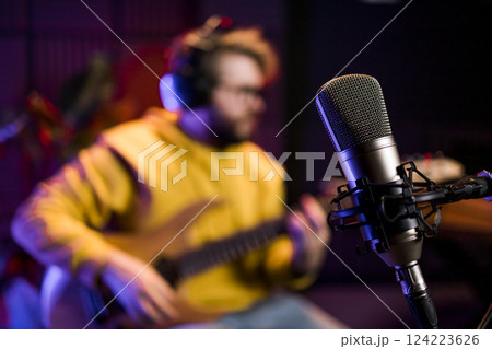 Male singer recording songs by using a studio microphone and and playing guitar in a music recording studio. Performance and show in the music business, streaming and recording music. 124223626