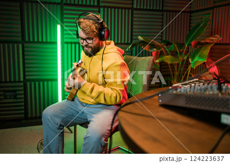 Male singer recording songs by using a studio microphone and and playing guitar in a music recording studio. Performance and show in the music business, streaming and recording music. 124223637