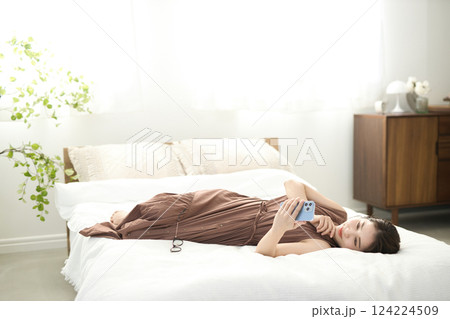 ベッドでくつろいでスマホを見る若い女性 124224509