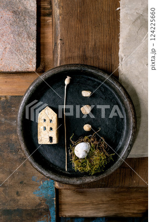 Close up black ceramic bowl with miniature ceramic house, small pebbles, moss nest with shell on rustic wooden background. Natural materials artistic composition with contrast textures. home concept Close up black ceramic bowl with miniature ceramic house, small pebbles, moss nest with shell on rustic wooden background. Natural materials artistic composition with contrast textures. home concept 124225660