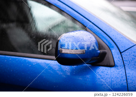 Close-up of a blue car side mirror with water droplets after rain, reflecting urban environment. 124226059