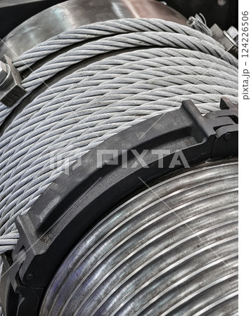 Industrial equipment showcases thick steel cables on a large spool in a workshop setting during daylight hours 124226506