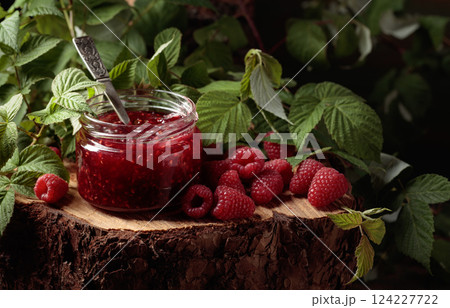 Jar of raspberry jam and fresh berries with leaves. 124227722