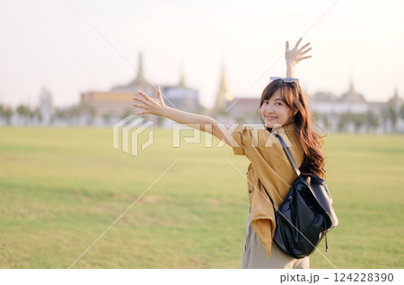 A Traveler Asian woman in 30s, bathed in golden glow of a Bangkok sunset, laughs with carefree joy, her arms outstretched as if to embrace freedom of the moment. Backpack strapped on. 124228390